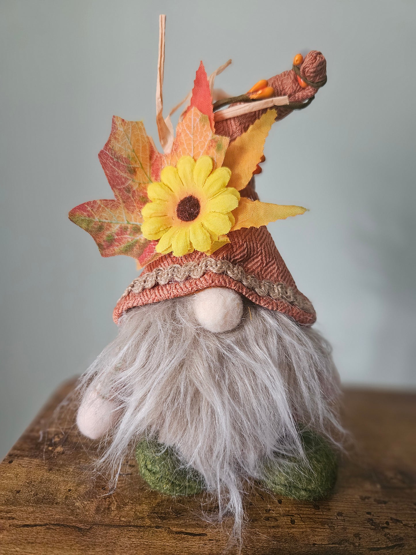 Gnome figurine with autumn leaves and a yellow flower on a wooden surface
