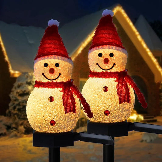 Two LED snowmen with red hats and scarves in front of a house with Christmas lights.