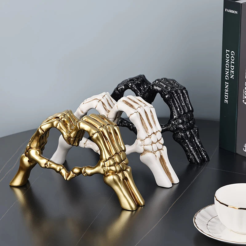 Decorative sculpture of skeletal hands forming a heart shape in gold, black, and white on a dark surface.