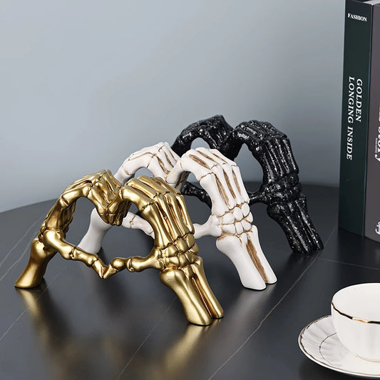 Decorative sculpture of skeletal hands forming a heart shape in gold, black, and white on a dark surface.