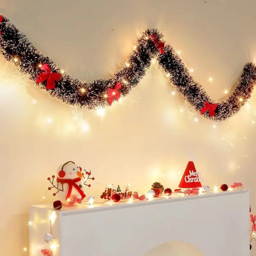 Decorative Christmas garland with lights and small ornaments on a white surface.