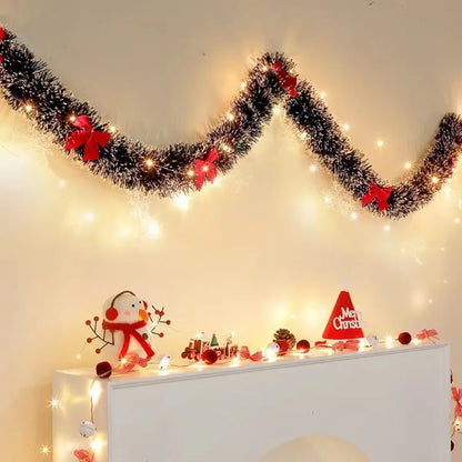 Decorative Christmas garland with lights and small ornaments on a white surface.