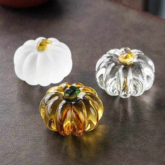 Three glass pumpkin decorations in white, clear, and gold on a dark surface.