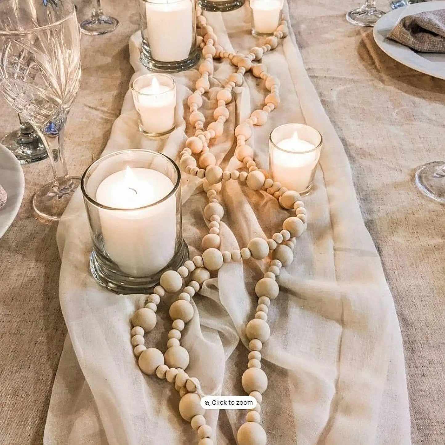 Decorative table setting with candles and a long wooden bead necklace on a beige cloth.